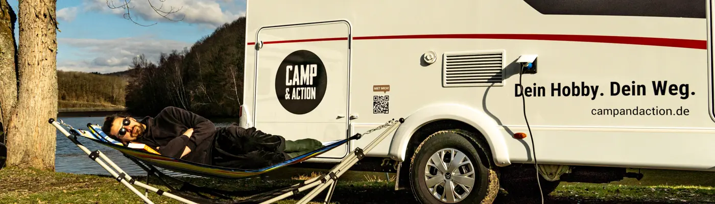 Mann in Haengematte vor Wohnmobil Sunlight A70 mit Camp and Action Logo
